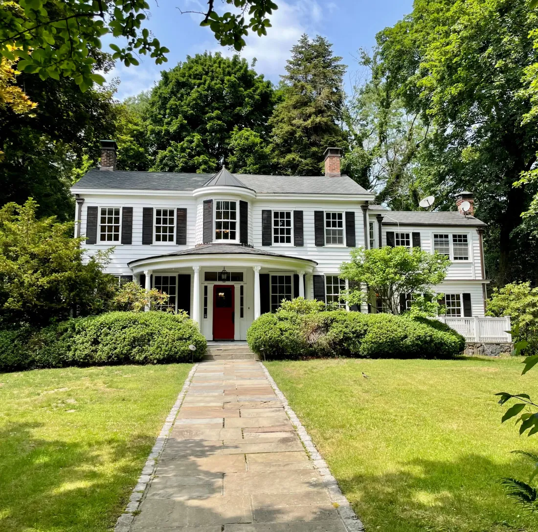 Front of the white colonial house with a red door and round porch