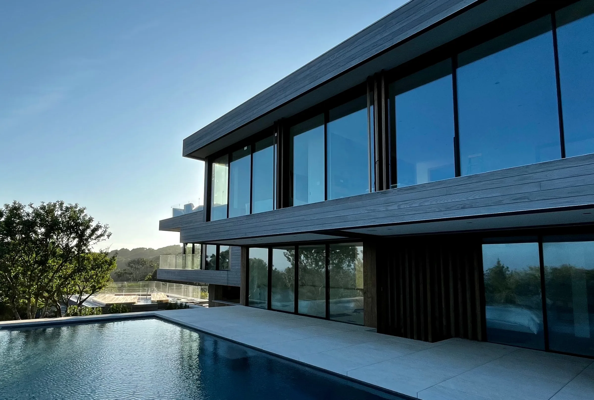 Modern two-storey home with an infinity pool and stone patio at sunset