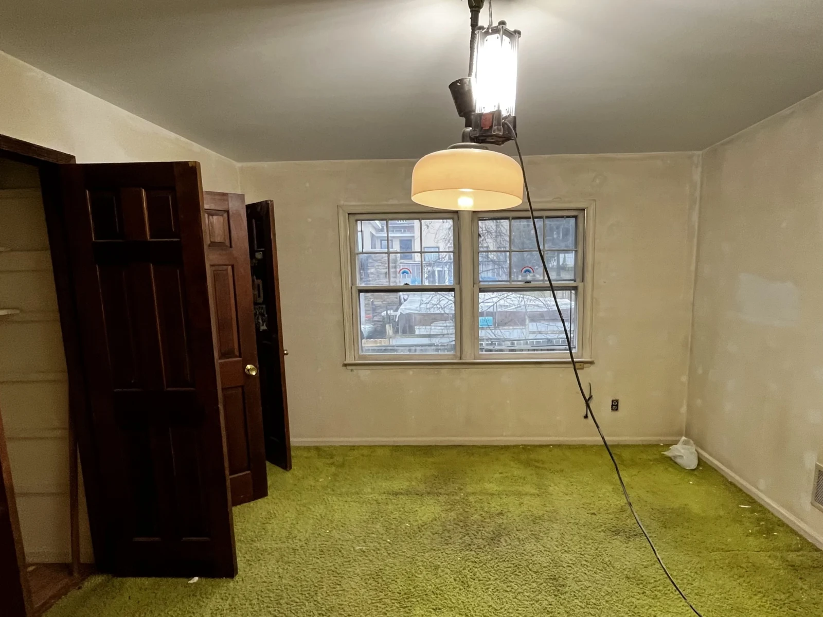Bedroom before: worn green carpet, patched walls and a hanging work light