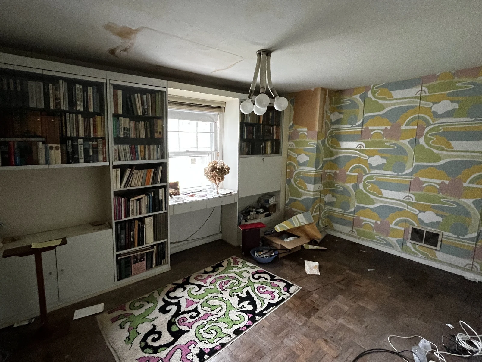 Office before: patterned wallpaper, crowded shelves and a stained ceiling
